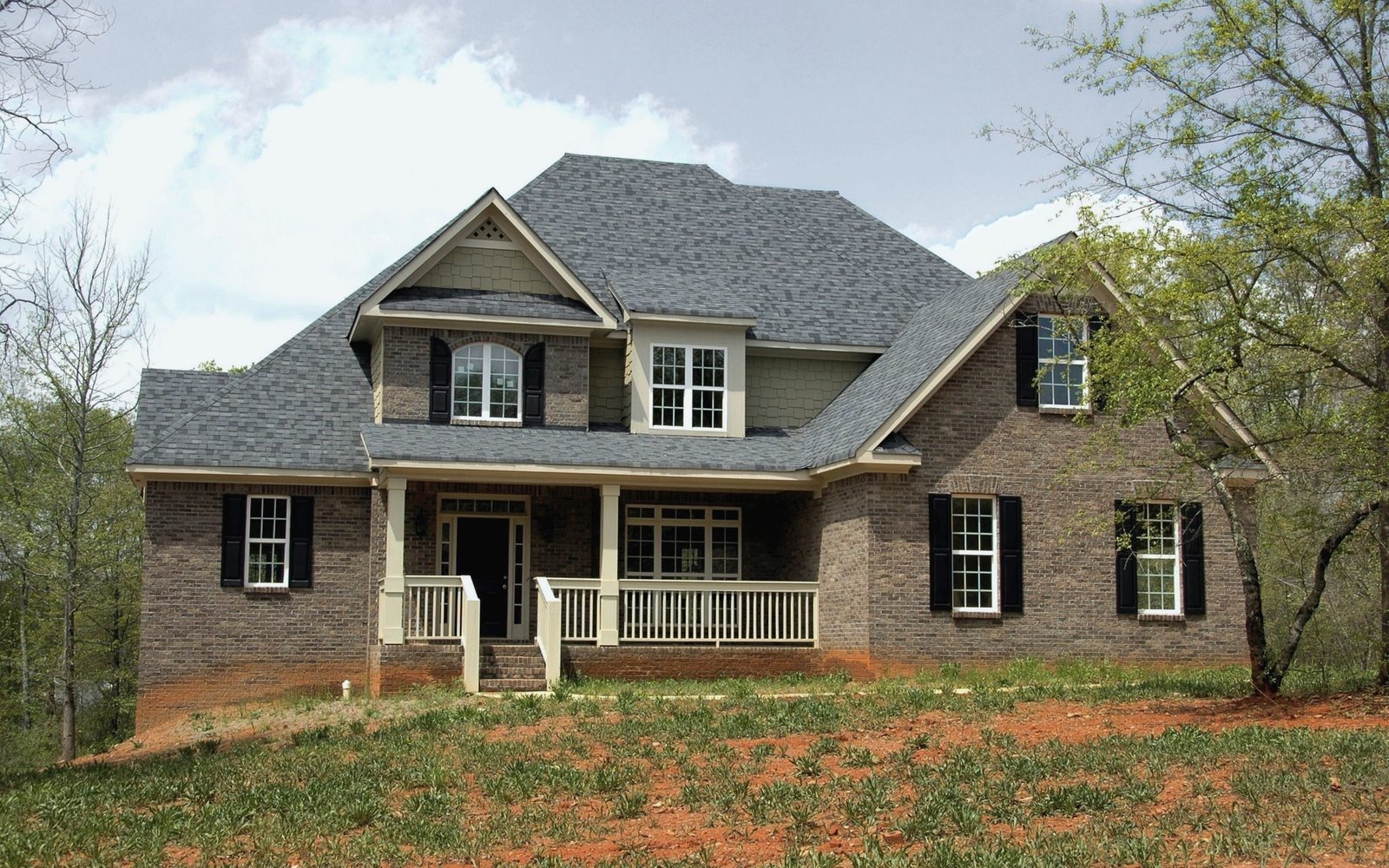 A steep architectural shingle roof with several gables on a brick two-story house
