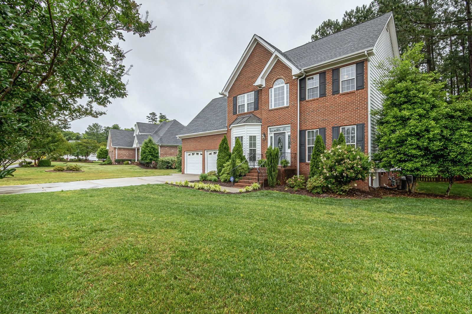 A brick two-story home with a finished architectural shingle roof under an overcast sky