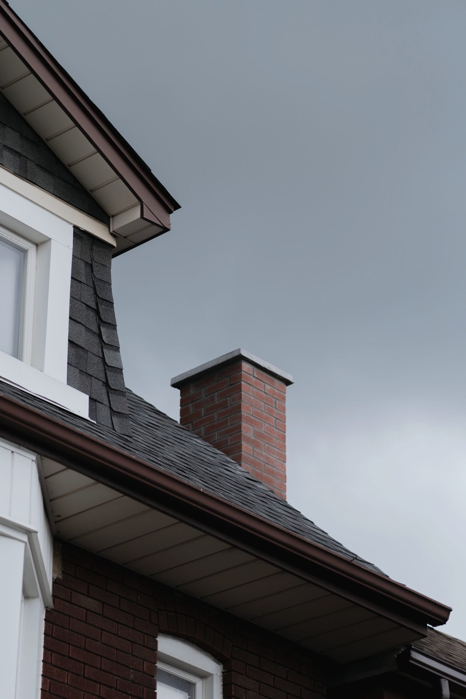 A dark shingle roof and brick chimney under a heavy gray sky
