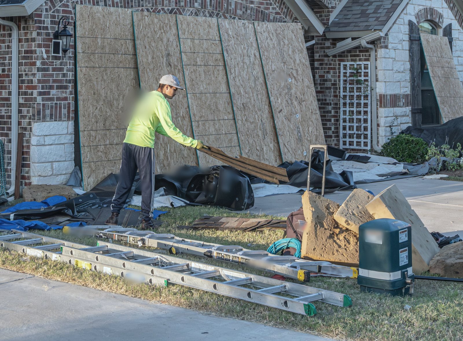 Tear-off day: a worker hauls old decking past boarded windows, ladders and tarps on the lawn
